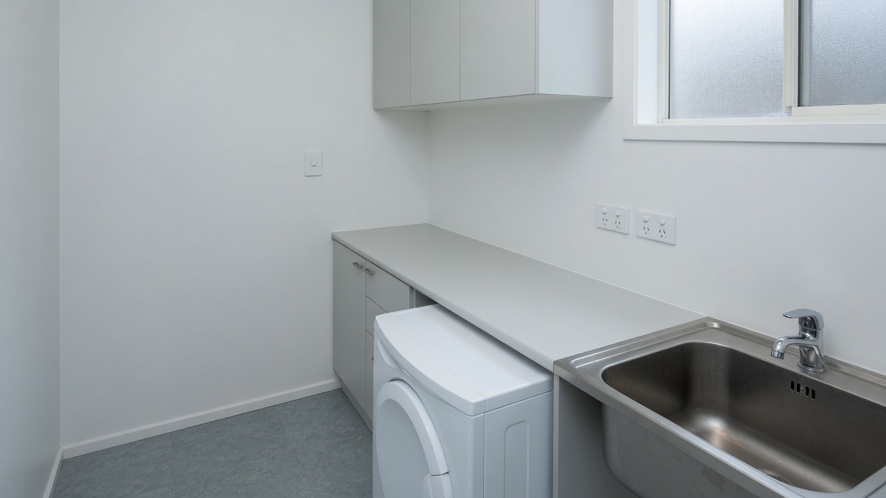 A generated placeholder image: a finished, empty New Zealand laundry with a light switch on the wall and two double outlets above the bench.