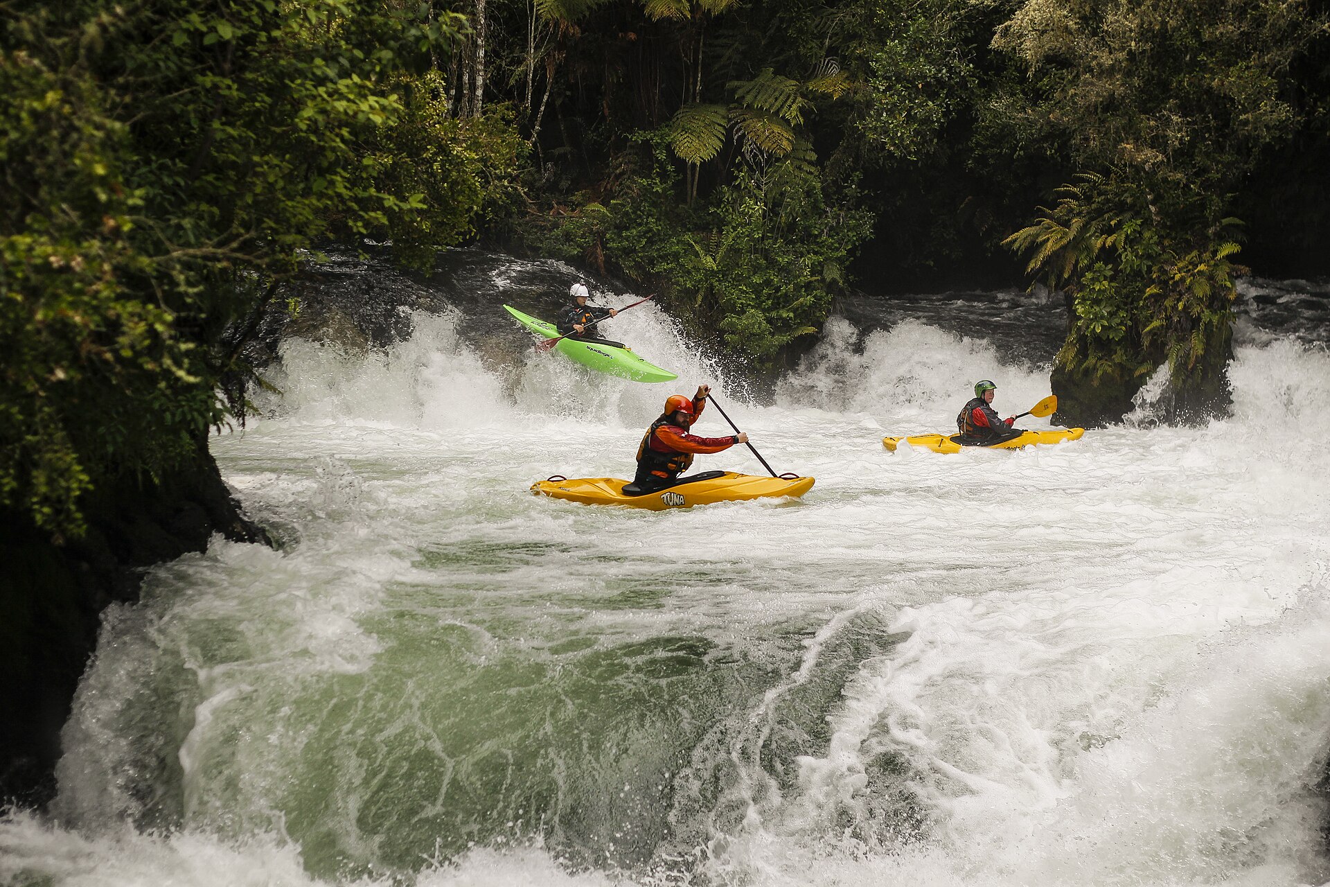 Three kayakers running a drop together on a whitewater river.