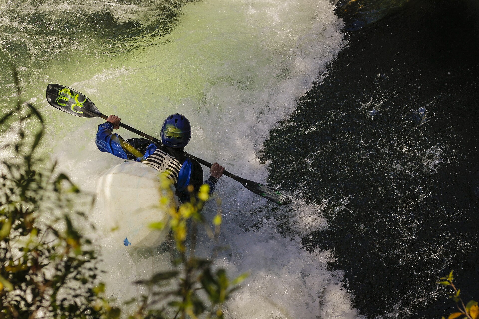 Seen over a paddler's shoulder, a kayaker drops into churning whitewater below.