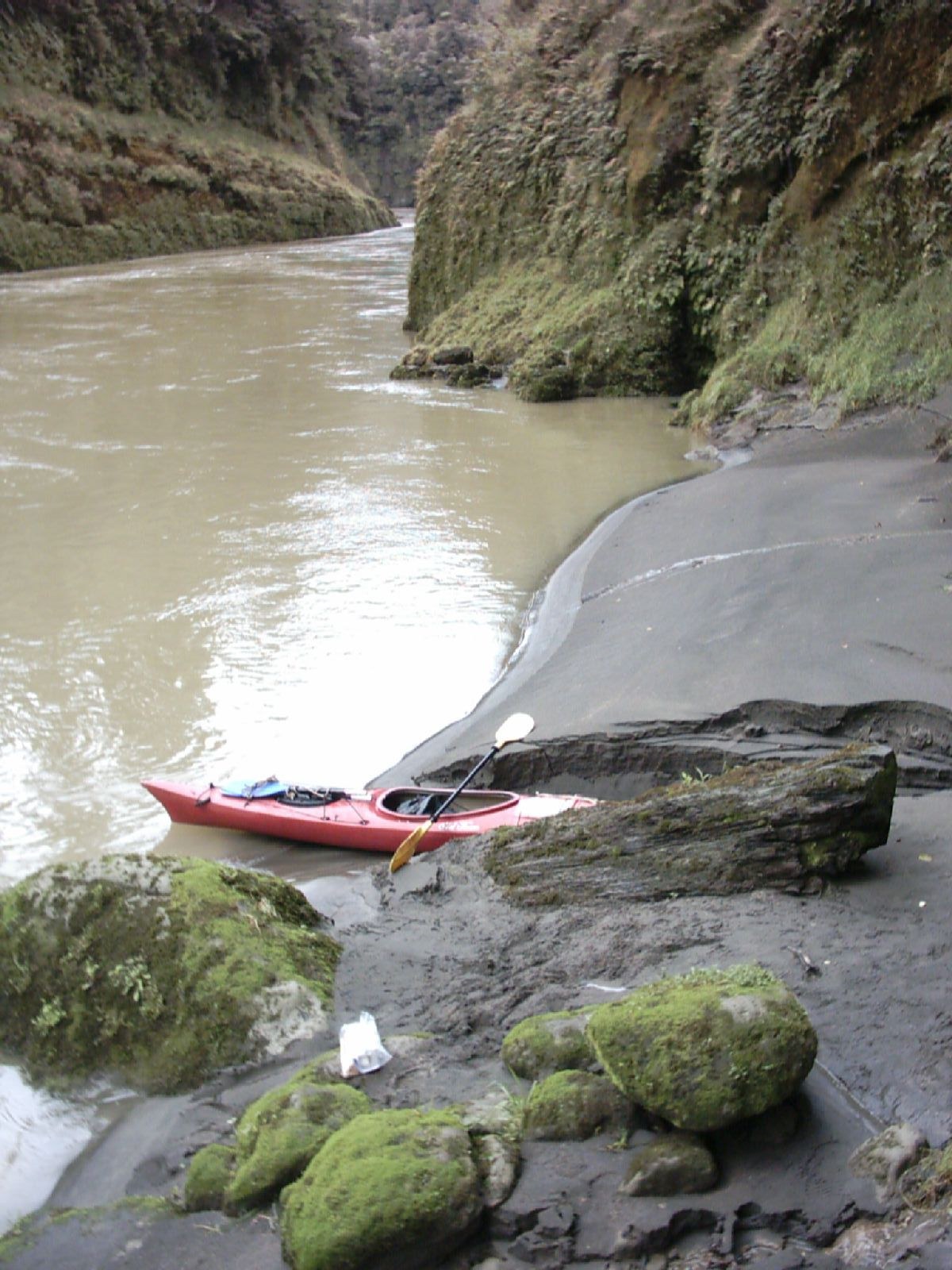 A touring kayak beached on the shore of a calm mudstone gorge.