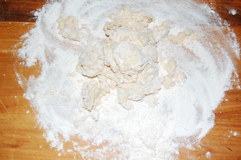 A rough ball of dough on a wooden bench, surrounded by a wide ring of scattered white flour.